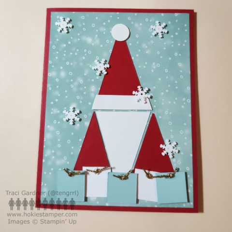 Front of a red greeting card, showing a snowy background with a red and white Santa gnome with presents at his feet.