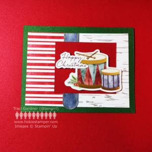 Happy Christmas card showing red & white striped paper and wood grain paper on a green base with a set of drums as the focal image